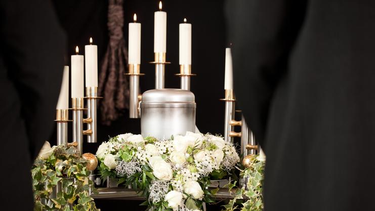 Kremationsurne inmitten von weißen Rosen und Kerzen, umgeben von einem grünen Blumengesteck.