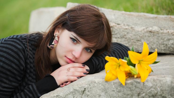 Junge Frau mit Blumen in der Nähe, die auf einem Stein liegt und in die Kamera schaut. Hintergrund mit grünem Gras.